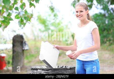 Giovane donna che lancia spazzatura in bidone di rifiuti all'aperto Foto Stock