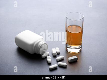 Bicchiere di alcol e bottiglia con pillole su sfondo grigio Foto Stock