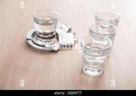 Bicchieri di alcol con manette su tavolo di legno. Concetto di dipendenza da alcol Foto Stock