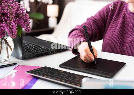 Il freelance di Graphic Designer retucher lavora da casa. La donna utilizza un tablet grafico in ufficio domestico utilizzando un notebook e un computer. Lavoro a distanza in un ambiente accogliente Foto Stock