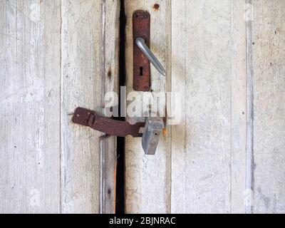 Parte di un antico esterno intemperato doppie porte con uno spazio. Superficie in legno verniciata bianca danneggiata, vecchia maniglia in ferro, foro per chiave vuoto, cerniera Foto Stock