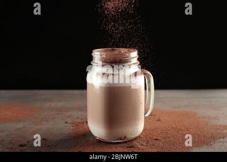 Versare la polvere di cannella in un vaso di mason con latte macchiato su fondo nero Foto Stock