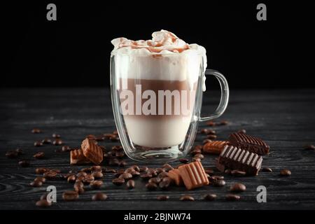 Bicchiere con caramello macchiato su tavolo su fondo nero Foto Stock