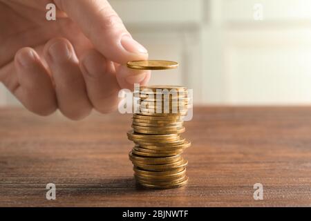 Donna che accatastano le monete su tavolo di legno, primo piano Foto Stock