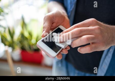 Uomo che utilizza un panno disinfettante su un telefono Foto Stock