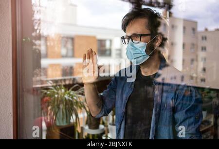Uomo con maschera facciale che guarda fuori dalla finestra Foto Stock