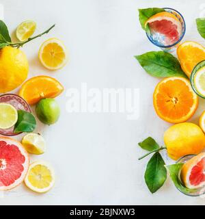 Cornice di agrumi vari con foglie verdi su tavolo bianco, vista dall'alto. Stile di vita sano. Ingredienti. Vitamina. Metà e sezioni. Layout Foto Stock