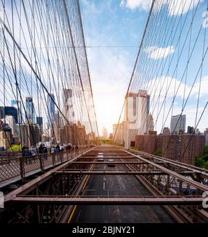 Guardando ad est dal Ponte di Brooklyn, di fronte ad un sole luminoso che sorge sopra i grattacieli in un cielo blu, con la strada sottostante e pedoni sul fondo Foto Stock