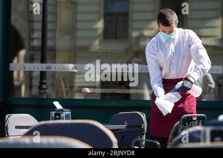 Il cameriere con maschera disinfetta il tavolo di un bar, caffetteria o ristorante all'aperto, riapre dopo le restrizioni di quarantena Foto Stock