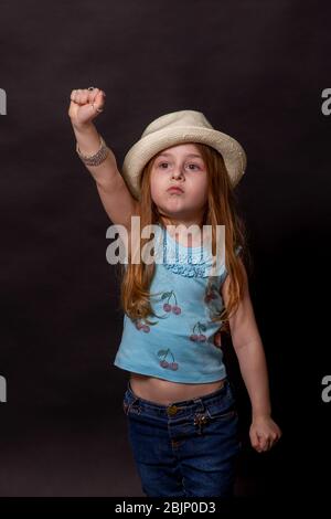 Bella ragazza che fa diverse espressioni: Braccia sollevate. Bambina su sfondo nero in jeans. Foto Stock