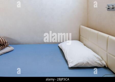 Il letto singolo è coperto da un foglio blu. Sul letto c'è un soffice cuscino bianco. Foto Stock