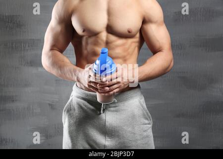 Giovane uomo sportivo con shake proteico su sfondo grigio Foto Stock