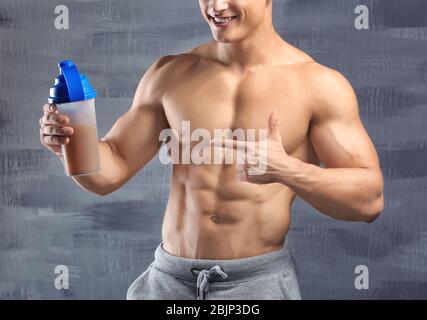 Giovane uomo sportivo con shake proteico su sfondo grigio Foto Stock