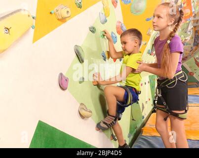 Adorabile ragazza che aiuta il fratellino a salire sul muro in palestra Foto Stock