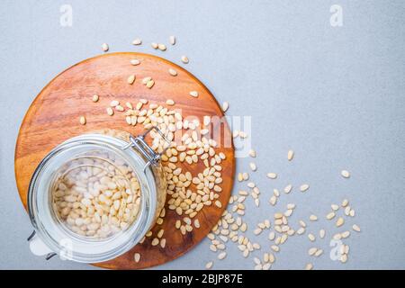 Vaso in vetro con cedro siberiano su un piedistallo in legno su sfondo grigio. Dadi sparsi sulla superficie. Alimenti vegetali organici ricchi di vitamina Foto Stock