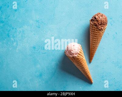 Varie gelato scoop in coni con copia spazio. Colorato di gelato in cono Cioccolato, fragola, mirtillo, pistacchio o matcha, biscotti al cioccolato cookie sandwich su sfondo blu. Vista superiore Foto Stock