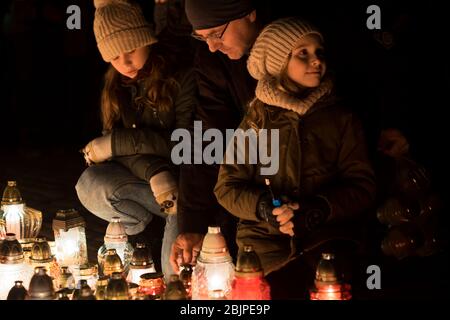 Un padre con due figlie accende una candela di fronte al monumento alle vittime polacche del comunismo al cimitero di Rakowicki a Cracovia, Polonia 2019. Foto Stock