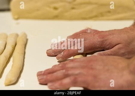 Gnocchi italiani freschi fatti in casa su un asse di legno infarinato in una cucina con basilico fresco dietro in una vista ravvicinata Foto Stock