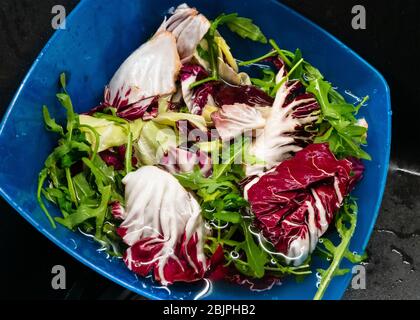Lavare con acqua la rucola e l'insalata di lattuga nel piatto di plastica blu da vicino. Foto Stock