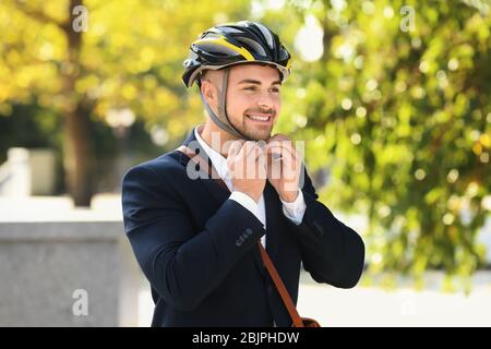 Giovane uomo d'affari bello che mette su casco di bicicletta all'aperto Foto Stock