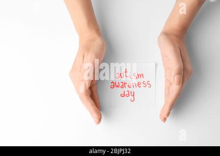 Donna che tiene le mani vicino al foglio di carta con il testo DI CONSAPEVOLEZZA AUTISMO GIORNO su sfondo bianco Foto Stock
