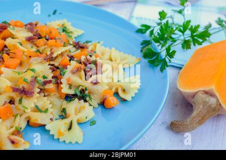 Farfalle di pasta integrale italiana con zucca di Butternut e prosciutto. Pasta con salsa di zucca, pancetta e prezzemolo fresco su sfondo di legno blu. IT Foto Stock