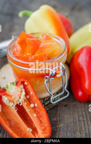 Peperone conservato in un vaso di vetro con peperoni freschi su fondo di legno vecchio. Marinato in casa con olio di pepe rosso. Vaso in vetro con arrosto conservato Foto Stock