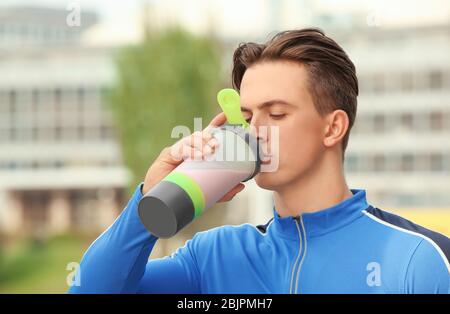 Giovane uomo sportivo che beve agitare proteine, all'aperto Foto Stock