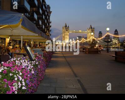 Serata a Londra con ristoranti completi lungo Butlers Wharf accanto al Tamigi con Tower Bridge sullo sfondo, Londra, Inghilterra, Regno Unito Foto Stock