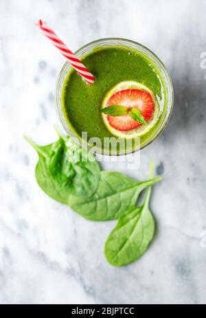 Vista dall'alto di un frullato di spinaci verdi con cornice di fragola e lime e una paglia da bere a righe rosse Foto Stock