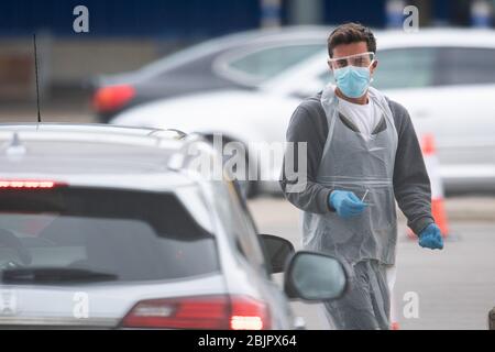 Un tester che indossa dispositivi di protezione individuale (PPE) tiene un tampone di prova in un viaggio attraverso il sito di test per coronavirus presso IKEA a Wembley, a nord di Londra. Foto Stock