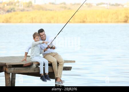 Padre e suo figlio pescano dal molo sul fiume Foto Stock