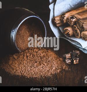 Vaso versato di noce moscata aromatica e bastoncini di cannella sulla pergamena vicino al filtro aggiunto spazio per il testo overlay Foto Stock