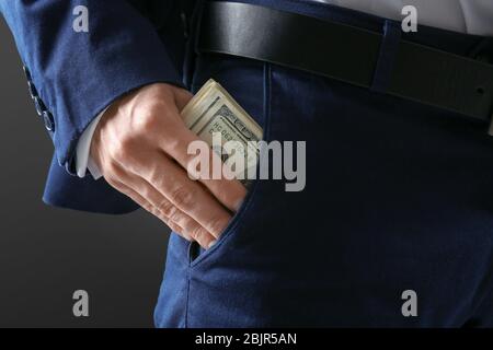 Uomo in abito formale mettendo i soldi in tasca su sfondo scuro, closeup Foto Stock