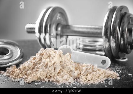 Mucchio di polvere di proteina con scoop e dumbbell sul tavolo, primo piano Foto Stock