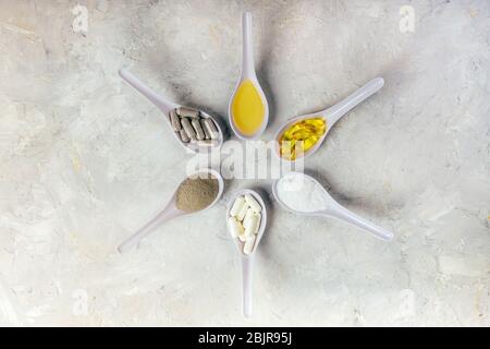 Capsule olio di pesce omega-3, piscine bianche e grigie, olio e polvere in cucchiai in cerchio su sfondo bianco rustico. Concetto di salute e bellezza. Foto Stock