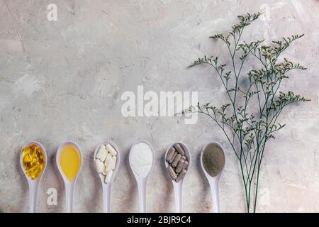 Capsule olio di pesce omega-3, piscine bianche e grigie, olio e polvere in cucchiai con diramazione di eucalipto su sfondo bianco rustico. Concetto di salute e bellezza. Foto Stock