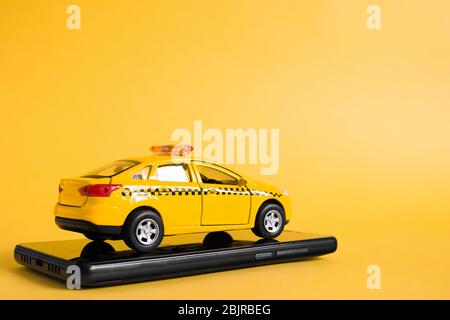 Concetto di applicazione online mobile per taxi urbani. Giocattolo giallo modello di taxi auto. Smartphone con funzione di trasporto taxi sul display. Mock up con copia Foto Stock