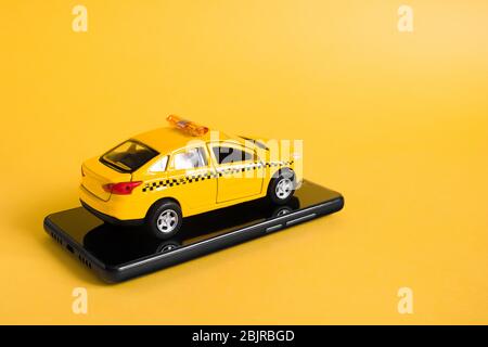 Concetto di applicazione online mobile per taxi urbani. Giocattolo giallo modello di taxi auto. Smartphone con funzione di trasporto taxi sul display. Mock up con copia Foto Stock
