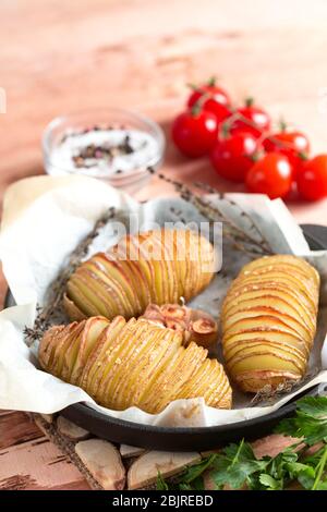Patate Hasselback. Patate al forno in padella su tavola di legno/ Foto Stock