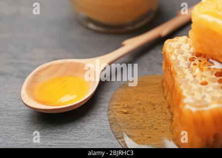 Cucchiaio di legno con miele su fondo grigio, primo piano Foto Stock