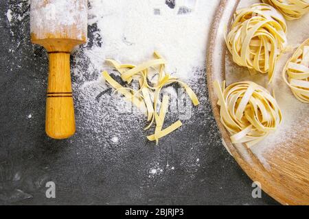 Varietà di spaghetti e tagliatelle di pasta cruda, fatti in casa, con farina su tavola di legno a dondolo per la pasta su pasta nera Foto Stock