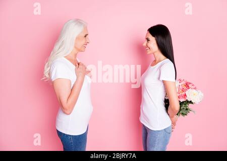 Foto di profilo di allegra madre giovane figlia donne passare il tempo insieme tenendo fiori freschi mazzo dietro indietro indossare magliette bianche jeans Foto Stock