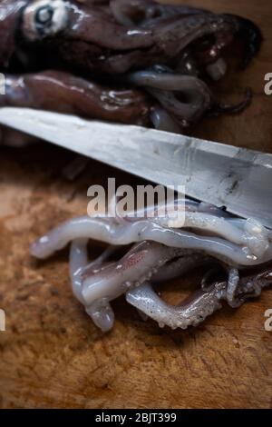 Calamari e tentacoli sul tagliere con coltello. Foto Stock