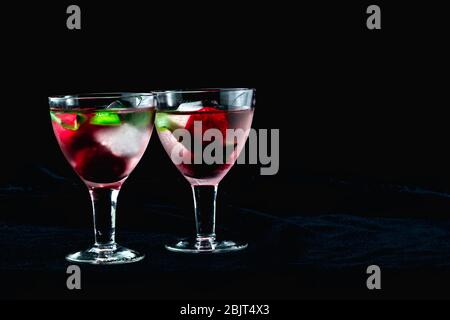 cocktail con fragole di ghiaccio ciliegie kiwi in bicchieri su uno sfondo nero Foto Stock