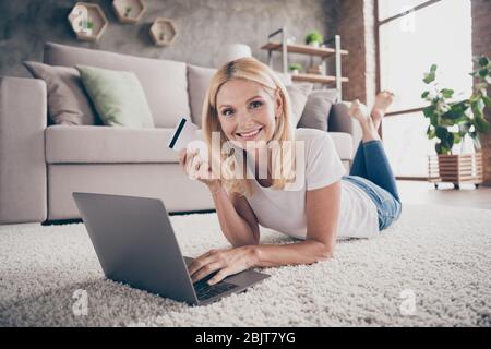 Ritratto di lei bella ragazza allegra e attraente sdraiato su tappeto utilizzando laptop e-banking servizio di pagamento consegna ordine merci in moderno loft mattoni Foto Stock