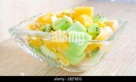 insalata sana per la colazione con banana e kiwi d'arancia in un piatto di vetro su un piatto di legno per il fitness. spazio per fotocopie Foto Stock