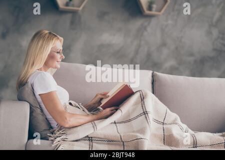 Profilo vista laterale ritratto di lei bella allegra piacevole ragazza matura seduta su divan lettura libro spendere buona vita giorno sogno in Foto Stock