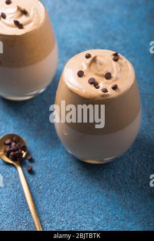 Il Dalgona Frothy Coffee è una bevanda sudcoreana con caffè istantaneo montato, zucchero e latte, su un tavolo di cemento blu Foto Stock