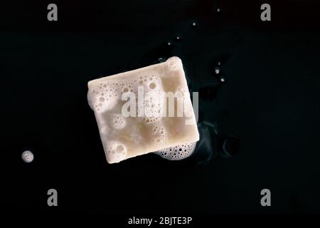 Saponetta con vista dall'alto su fondo nero con suds in schiuma. Schiuma naturale di olio di oliva fai da te con struttura a bolle di schiuma. Lavaggio delle mani con sapone per igiene personale COVID-19 prevenzione. Foto Stock